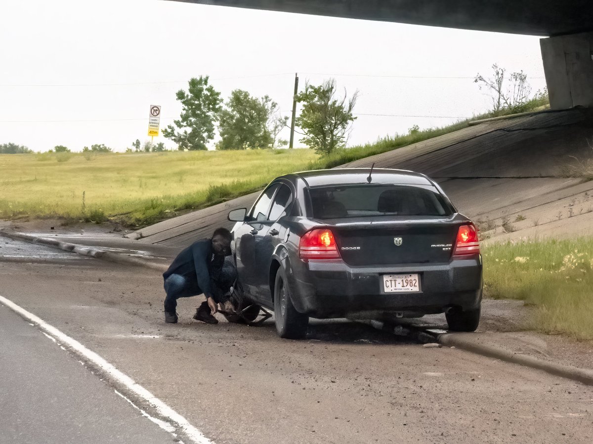 Professionnel mechanic kneeling beside an SUV changing a tire on the side of a road